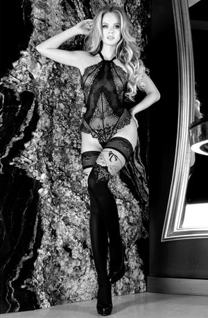 Black and white image of a woman leaning against a marble wall. She is wearing lacy lingerie with thigh-high Ballerina 555 Black/Skin Hold Ups from the Gold Elixir Collection and high heels. Her long, wavy hair cascades over her shoulders, with one hand on her hip and the other resting above her head.