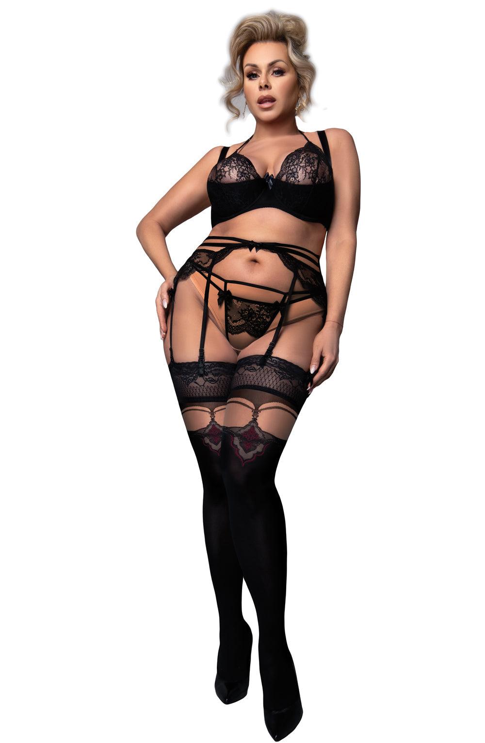 A person with blonde hair is posing in the Ballerina 602 Black/Skin Hold Ups Plus, a black lace lingerie set featuring a bra, garter belt, panties, and thigh-high stockings made from premium materials with intricate lace details near the top. The individual is also wearing black high-heeled shoes.