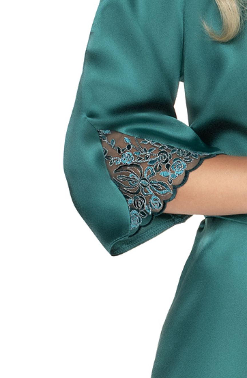 A close-up of an arm in the Irall Emerald Dressing Gown Green reveals a teal, satin-like fabric with an embroidered lace detail at the sleeve end. The intricate floral pattern embroidery adds elegance, and the silky material has a slight sheen. The arm is crossed over the body, reminiscent of luxurious satin dressing gowns by Irall.