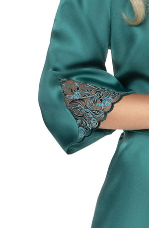 A close-up of an arm in the Irall Emerald Dressing Gown Green reveals a teal, satin-like fabric with an embroidered lace detail at the sleeve end. The intricate floral pattern embroidery adds elegance, and the silky material has a slight sheen. The arm is crossed over the body, reminiscent of luxurious satin dressing gowns by Irall.