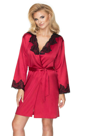 A woman with blonde hair is wearing the Irall Juniper Burgundy Dressing Gown by Irall, which features a satin finish and black lace trim on the collar and sleeves. She is standing and looking directly at the camera with a slight smile. The dressing gown is elegantly tied at the waist with a matching silk belt.