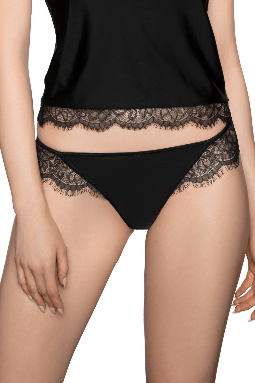 A person is shown from the shoulders down wearing a black, satin camisole and the Roza Erii Black Thong by Roza. Both garments feature delicate eyelash lace trim, and the person's hands rest near their hips.