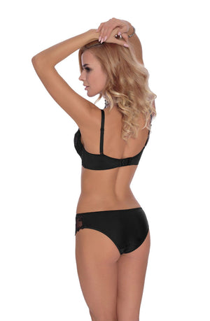 A blonde woman with wavy hair is shown from the back, standing with her arms raised and hands resting on her head. She is wearing the Roza Kalisi Soft Cup Bra Black and matching panties, both adorned with delicate floral embroidery. She has a slender figure and light skin.