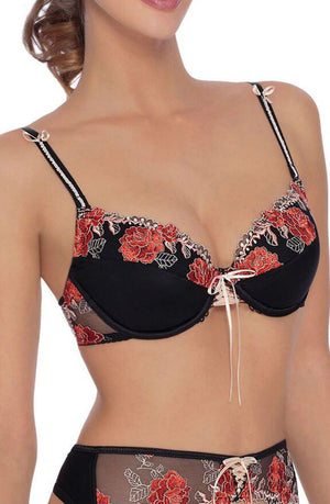 A woman wearing the Roza Natali Black Bra and matching panties set, adorned with red and white floral embroidery. The bra from Roza features thin straps with small bow details and a front lace-up detail, while the coordinating panties include sheer fabric with similar floral embroidery, creating an exquisite, coordinated look.