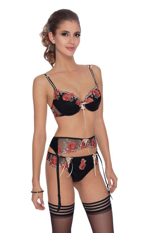 A woman with light skin and long brown hair is modeling black lingerie by Roza, featuring red and white floral embroidery. She is wearing a matching bra, garter belt, and the Roza Natali Black Thong, paired with black stockings. She stands against a plain white background.