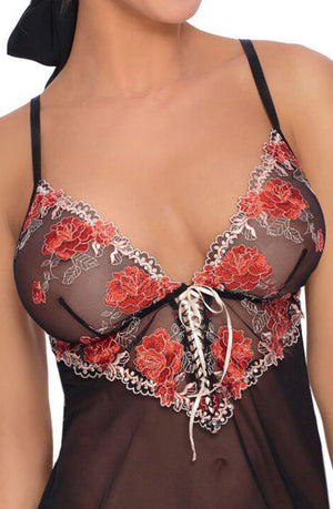 A woman is wearing a sheer black lace Roza Natali Chemise with thin straps and red floral embroidery on the bust. This piece from the Roza collection features a plunging neckline with white lace-up detailing in the center. The woman's face is partially visible.