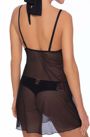 A person is wearing a sheer black Roza Natali Chemise from behind. The Roza garment, adorned with delicate embroidery, has thin straps and falls loosely around the upper thigh. They are also wearing coordinating black underwear underneath. Their hair is tied up with a black ribbon.