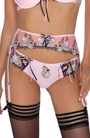 A person wearing the Roza Natali Pink Thong by Roza, a pink lingerie set with black lace trim and floral embroidery. The ensemble includes a bra and panty with black laced details, as well as a garter belt with attached stockings adorned with black horizontal stripes. The individual is standing, their head not visible.