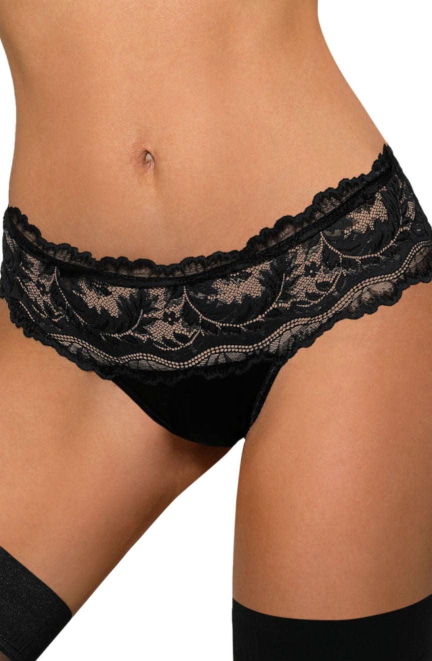 A person wears the Roza Sefia Thong Black, featuring an intricate floral design and scalloped edges enhanced by a satin ribbon detail, paired with black thigh-high stockings, standing against a plain background.