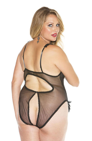 A woman with long blonde hair models the Shirley Of Hollywood X2497 Black Teddy by Shirley of Hollywood. The sheer plus-size lingerie bodysuit features cutout sections at the back. She is posing with her back to the camera and looking over her shoulder, wearing red lipstick and dangling earrings.