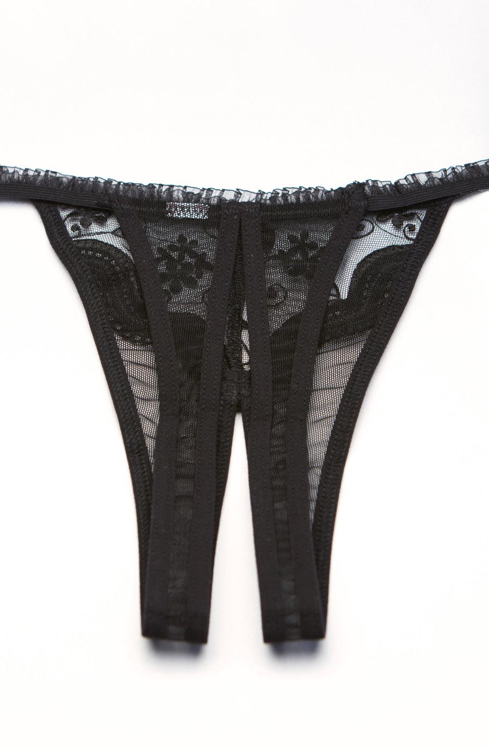 A close-up view of the Shirley Of Hollywood 10 Crotchless Thong Black by Shirley of Hollywood, lying flat on a white surface. The thong showcases two symmetrical straps connected by sheer fabric adorned with intricate lace detailing and scalloped embroidery, creating a stylish and delicate appearance.