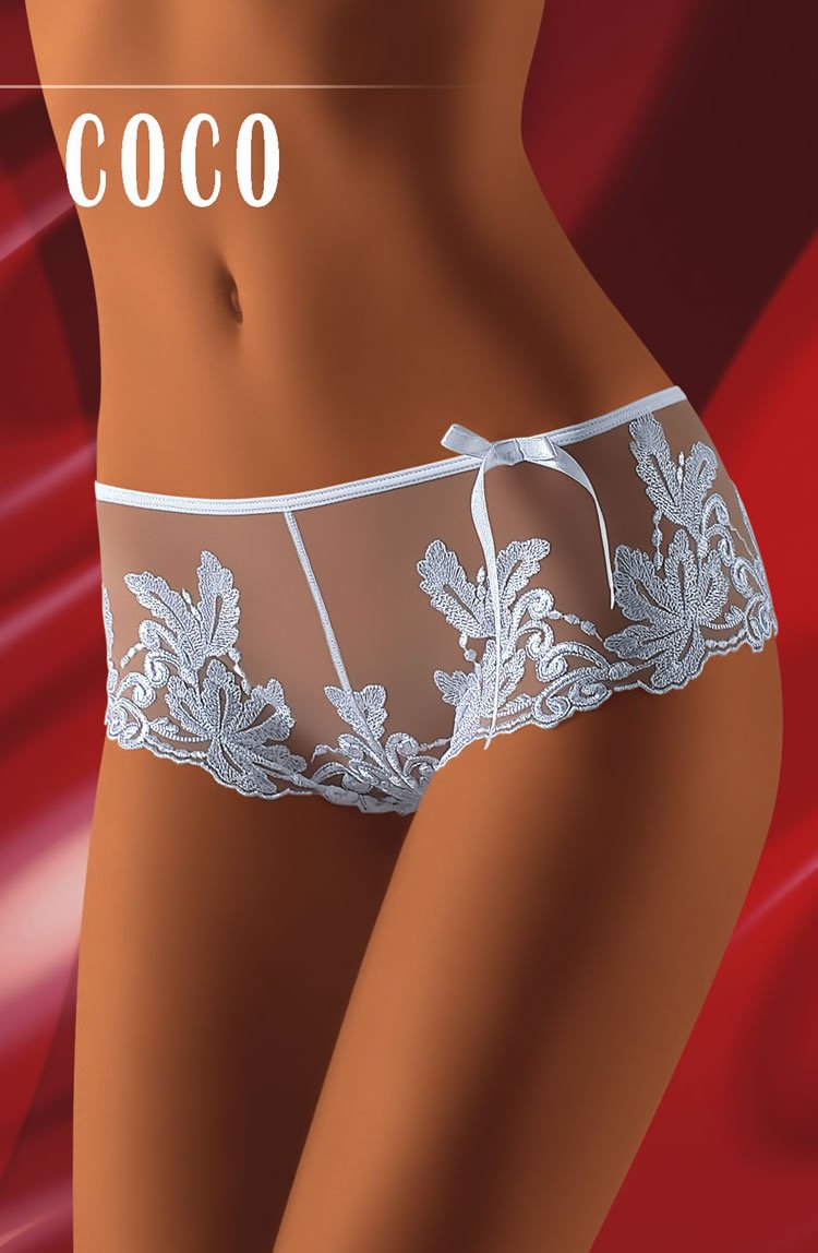 A model wearing intricate, lace-embroidered Wolbar Coco White Shorts with leaf patterns on a red background. The word "COCO" is written at the top of the image in bold, white letters. These delicate shorts from Wolbar make for a charming gift option.
